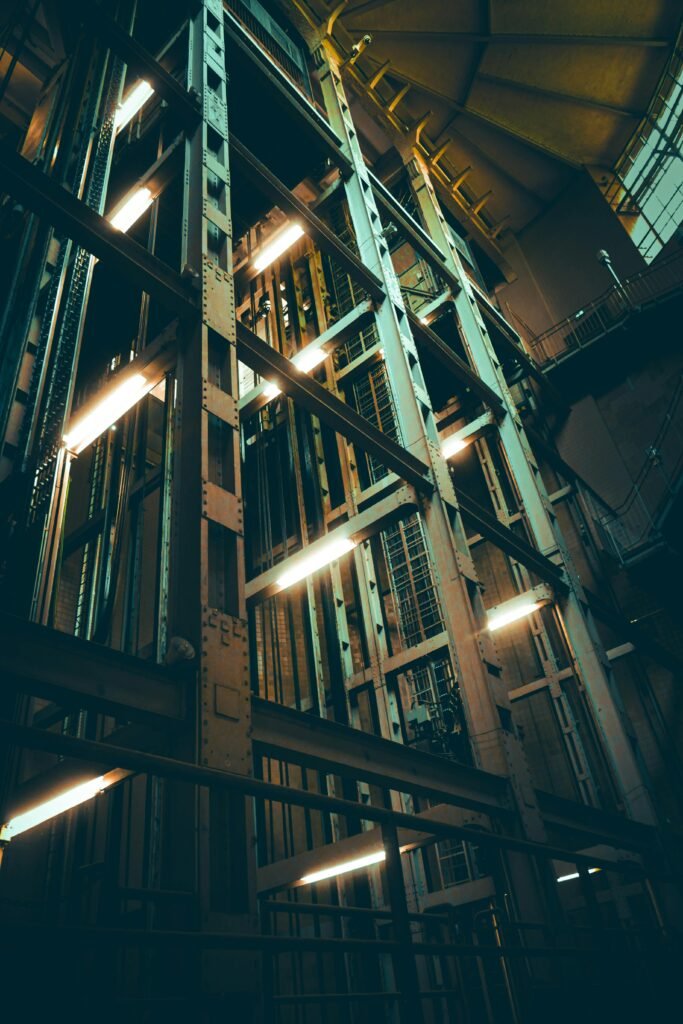A towering view of an industrial elevator shaft illuminated with glowing lights, displaying engineering complexity.